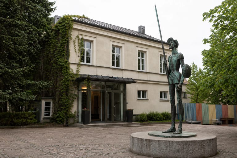 Žalvarinis Don Kichotas su ilga ietimi Panevėžio teatro „Menas“ kieme prie šviesaus istorinio pastato