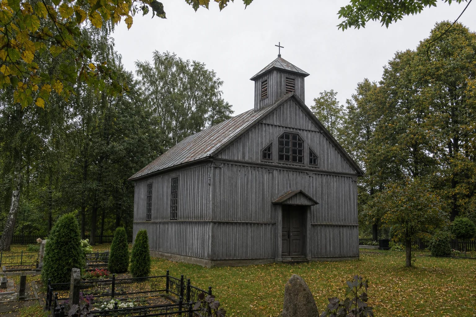 Small weathered wooden Parausiai Village Chapel of the Sacred Heart of Jesus with a square belfry and cross beside a rural cemetery