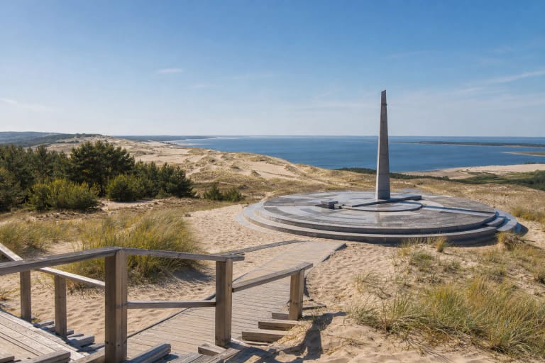 Parnidis Dune in Nida with the sundial obelisk, wooden path, white sand, and Curonian Lagoon horizon