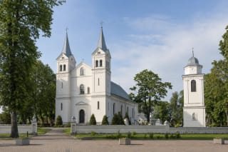 Pasvalys Church of St John the Baptist with twin towers, bell tower, and churchyard trees on Vytauto Didžiojo Square