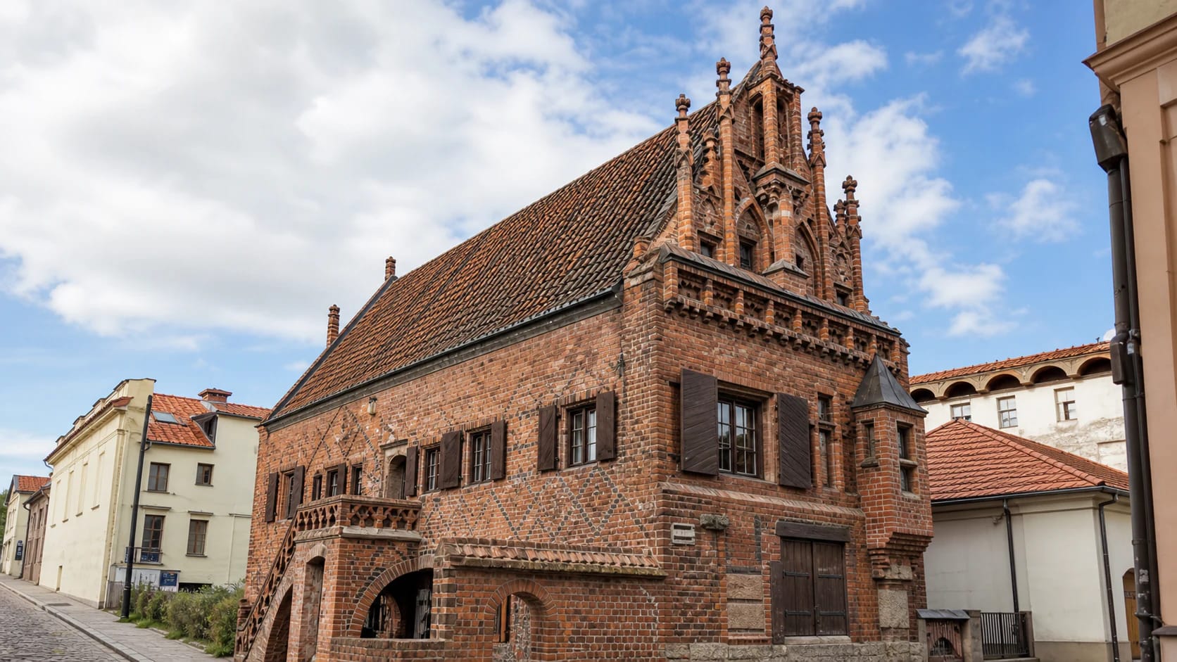 Red-brick Gothic facade of the House of Perkūnas in Kaunas with steep tiled roof, ornate gable, black-brick ornament, and wooden shutters