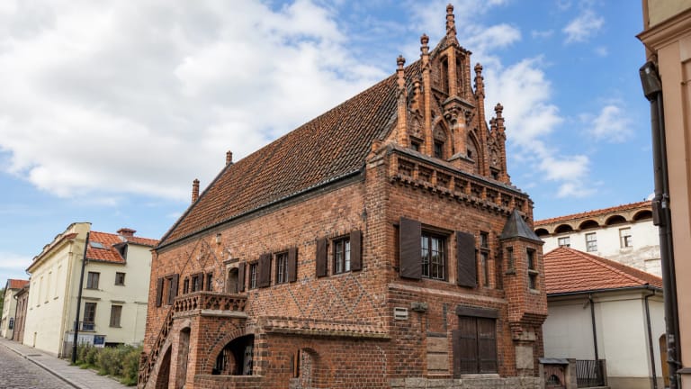 Perkūno namo Kaune raudonų plytų gotikinis fasadas su stačiu čerpiniu stogu, puošniu frontonu, juodų plytų ornamentu ir medinėmis langinėmis