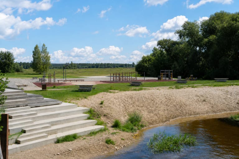 Piniavos laisvalaikio zonos smėlinga Lėvens pakrantė, betoniniai laiptai ir raudonos dangos lauko treniruoklių aikštelė