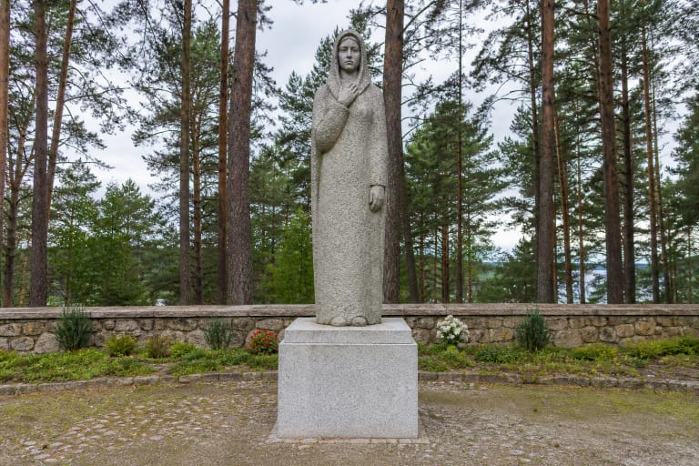 Granitinė Pirčiupių Motinos skulptūra žolėtoje memorialo aikštėje prie pušyno