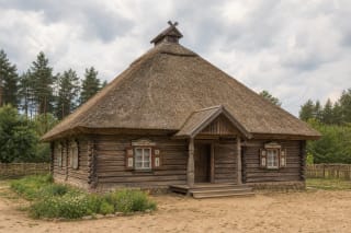 A traditional Dzūkija pirkia with log walls, hipped roof with smoke vent, shutters, and a small porch