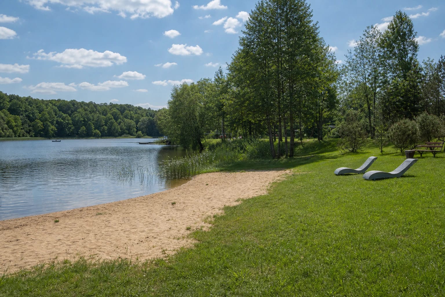 Plinkšiai Recreation Area's sandy shore, lawn, and two metal loungers beside the lake