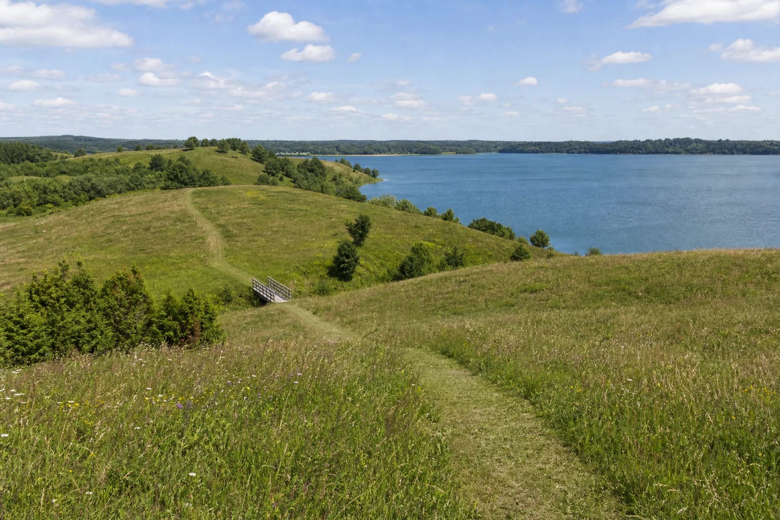 Prelomčiškės kalvų pažintinio tako pieva su taku, tilteliu ir plačia Dusios ežero panorama