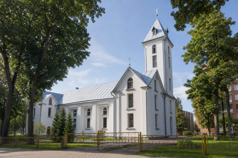 Balta Radviliškio Švč. Mergelės Marijos Gimimo bažnyčia su vienu centriniu bokštu, skardiniu stogu ir medžiais miesto šventoriuje