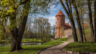 Raudonė Castle Park with the red-brick castle tower, old trees, and a path