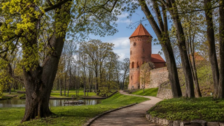 Raudonės pilies parkas su raudonų plytų pilies bokštu, senais medžiais ir taku