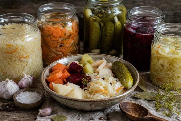 Assorted vegetables fermenting for winter with cabbage, carrots, beets, and cucumbers in clay vessels, with caraway and cranberries nearby