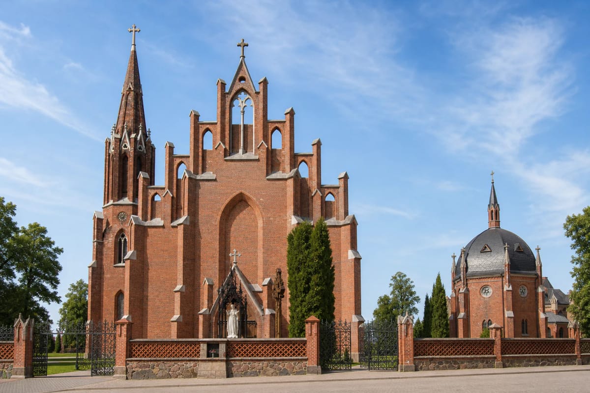 Stepped red-brick façade, tall side bell tower, and St Joseph's Chapel at the Church of St Matthew in Rokiškis on a sunny day