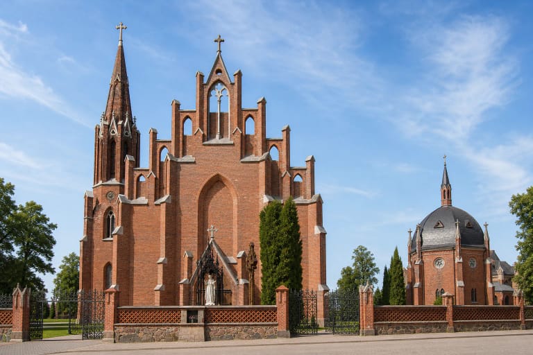 Rokiškio Šv. Mato bažnyčios raudonų plytų laiptuotas fasadas, aukšta šoninė varpinė ir Šv. Juozapo koplyčia saulėtą dieną