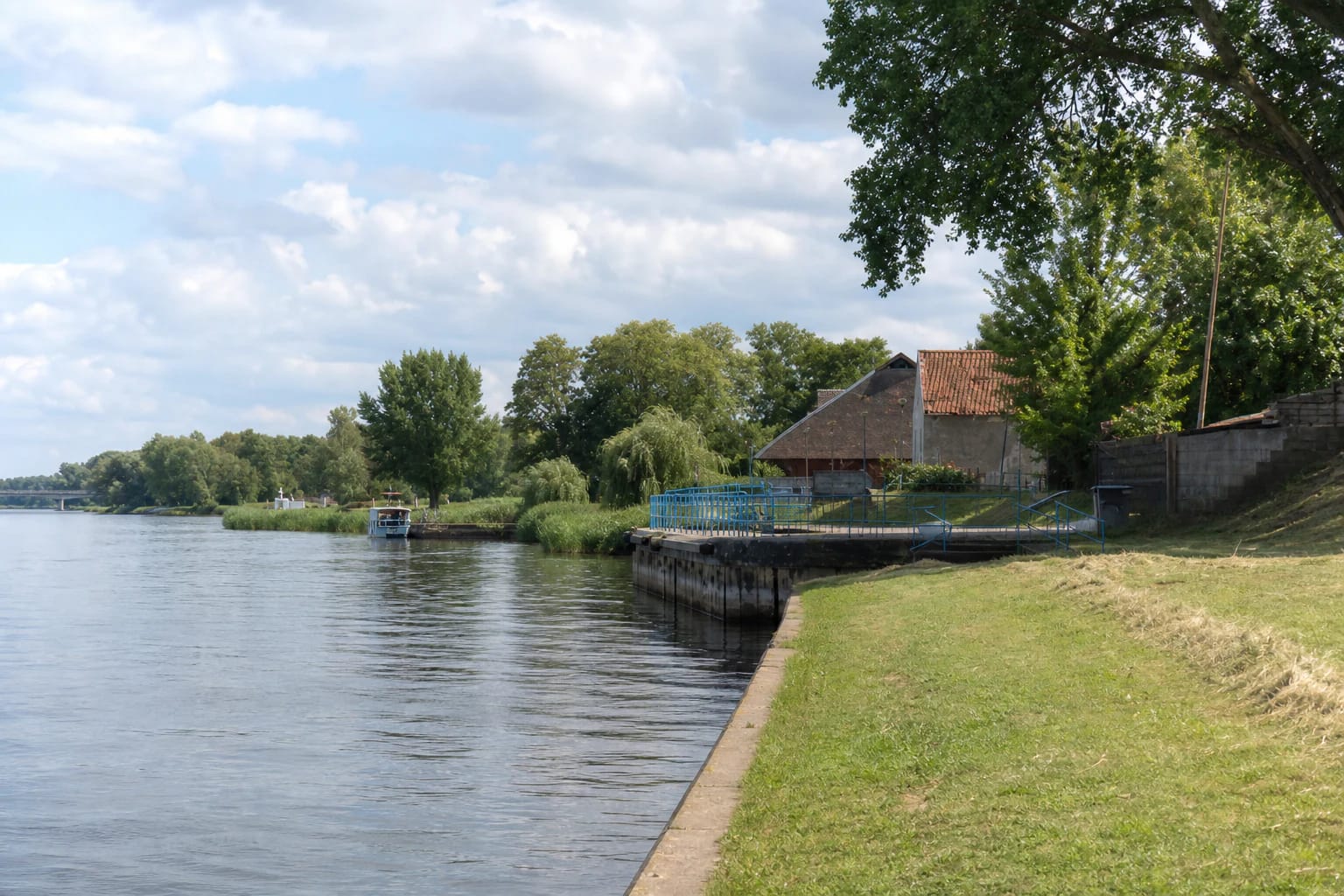 Rusnė Pier on the Atmata, with a low concrete quay, blue railings, and the flat delta landscape