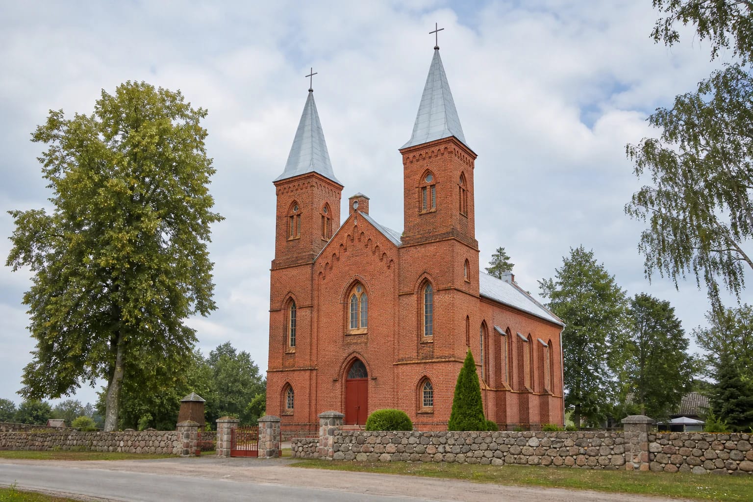 Šatės Church of St John the Baptist with two red-brick towers and a stone churchyard fence