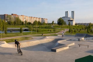 Бетонная площадка для скейтбординга и BMX в парке Саюдиса, окружённая зелёными газонами, дорожками и многоэтажками южной Клайпеды