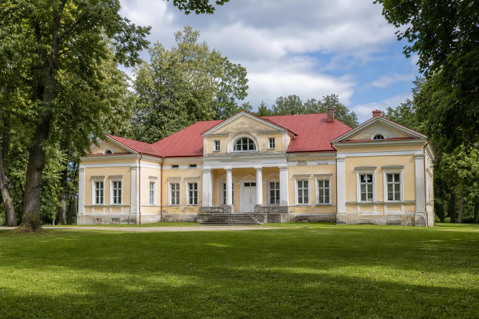 Yellow Classical Saldutiškis Manor palace with red roof and park trees