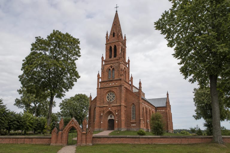 Šateikių Šv. evangelisto Morkaus bažnyčios raudonų plytų fasadas, aukštas smailus bokštas ir neogotikiniai vartai