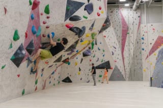 Laipiotojas ant spalvotais kybiais ir juodomis formomis nusėtos „Scala Dream“ boulderingo sienos