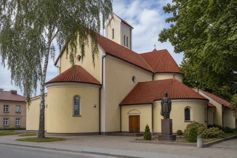 Šviesi Šiaulių Šv. Ignaco Lojolos bažnyčia raudonų čerpių stogais ir šventojo skulptūra kieme