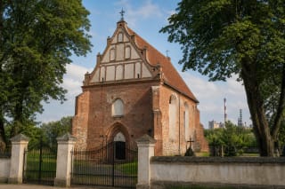Skarulių Šv. Onos raudonų plytų bažnyčia šventoriuje su pramonės bokštais tolumoje