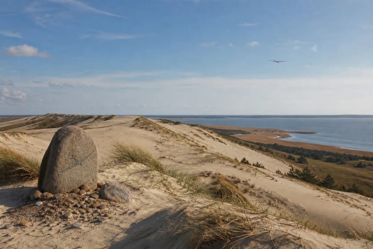 Sklandytojų kopa prie Nidos su atviru smėlio gūbriu, Kuršių marių horizontu ir sklandymo istoriją menančiu ženklu
