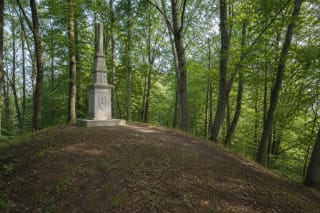 Покрытый лесом вал и бетонный памятник 1928 года на городище Скомантай