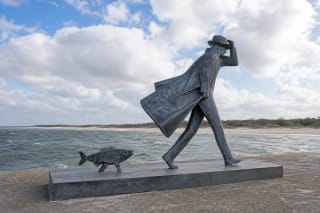 Separate steel silhouettes of a person and fish on the Melnragė pier beside the sea