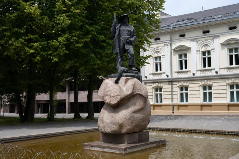 Dark bronze Fisherman sculpture on a carved pink boulder in a fountain beside Klaipėda City Hall