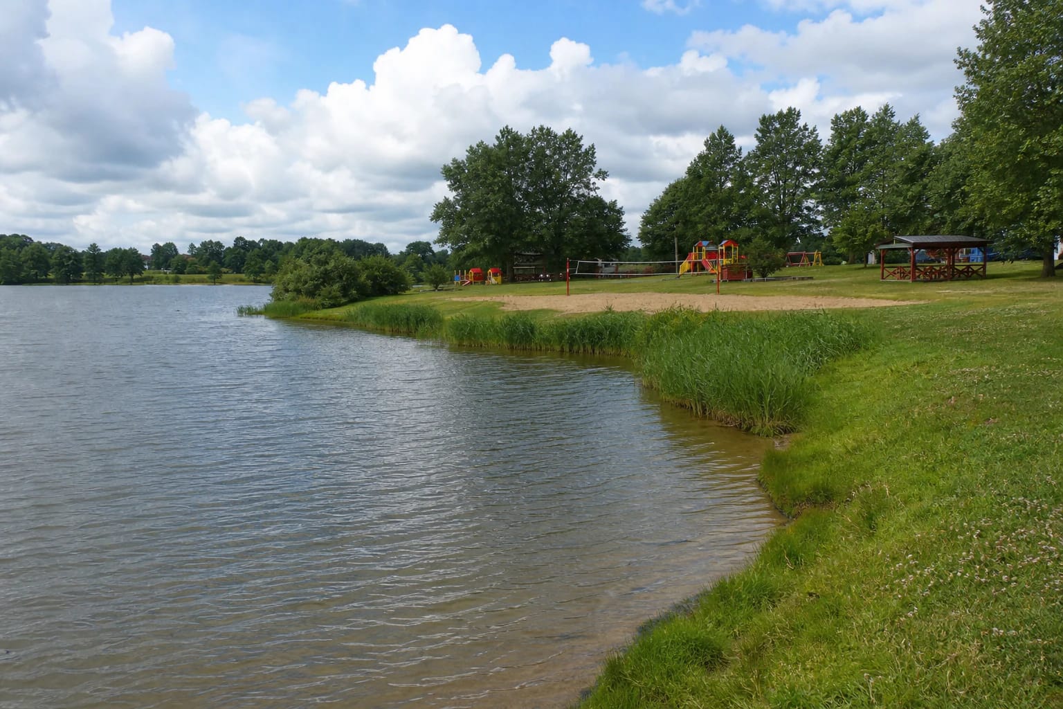 Skuodas Reservoir Beach with a sand strip, grassy shore, and recreation facilities