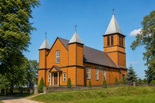 Оранжевый деревянный костёл Святой Анны в Славикае с двумя башенками, колокольней и зелёным двором