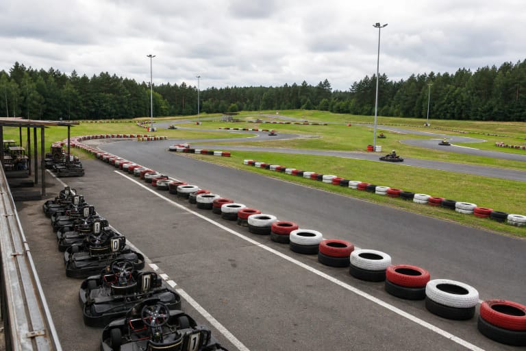 Извилистая асфальтовая трасса открытого картодрома Speedway с цветными шинными ограждениями, картами и лесом на краю