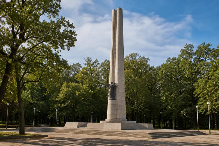 Tall tapering granite Darius and Girėnas Monument with a bronze composition among the trees of Ąžuolynas in Kaunas