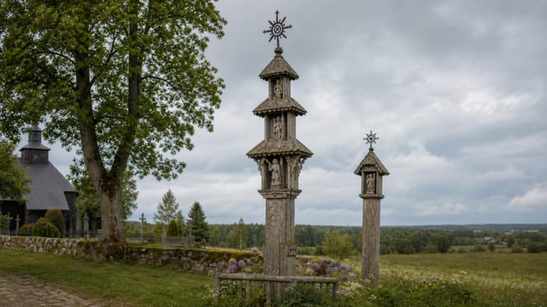 A Lithuanian wooden roofed pillar shrine with carved figures and a forged sunburst top