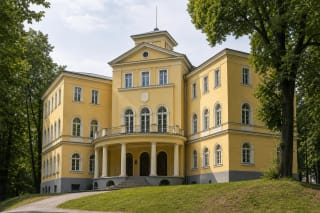 Yellow historicist facade of the Neo-Lithuania Student Corporation Palace in Kaunas with a columned terrace, balcony, pediment, small tower, and trees on Parodos Hill