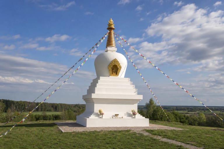 Balta Stupkalnio budistinė stupa su auksine smaile ir spalvotomis maldos vėliavėlėmis ant žalios kalvos