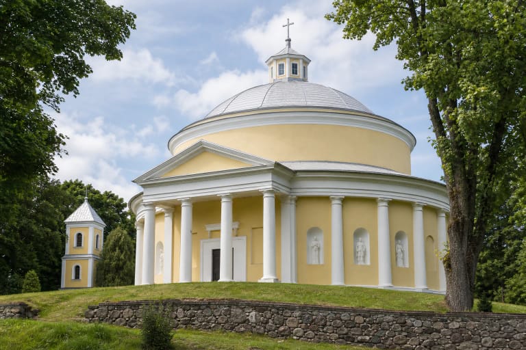 Circular pale-yellow Church of the Holy Trinity in Sudervė with a white Doric colonnade and silver dome