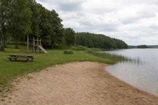 Пляж водохранилища Суйняй с песчаной полосой, игровой зоной, травой и спокойным берегом, поросшим деревьями