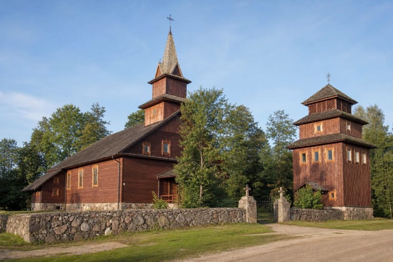 Ruda medinė Baltriškių Šv. Kazimiero bažnyčia su bokštu, varpais ir akmenine tvora