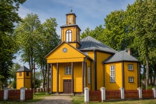 Жёлтый деревянный костёл Швентежериса с четырёхколонным портиком, ступенчатой башней и отдельной звонницей в зелёном церковном дворе