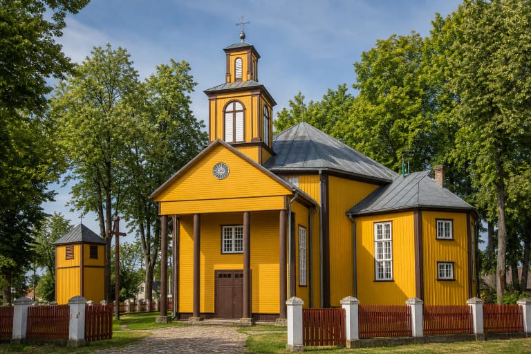 Жёлтый деревянный костёл Швентежериса с четырёхколонным портиком, ступенчатой башней и отдельной звонницей в зелёном церковном дворе