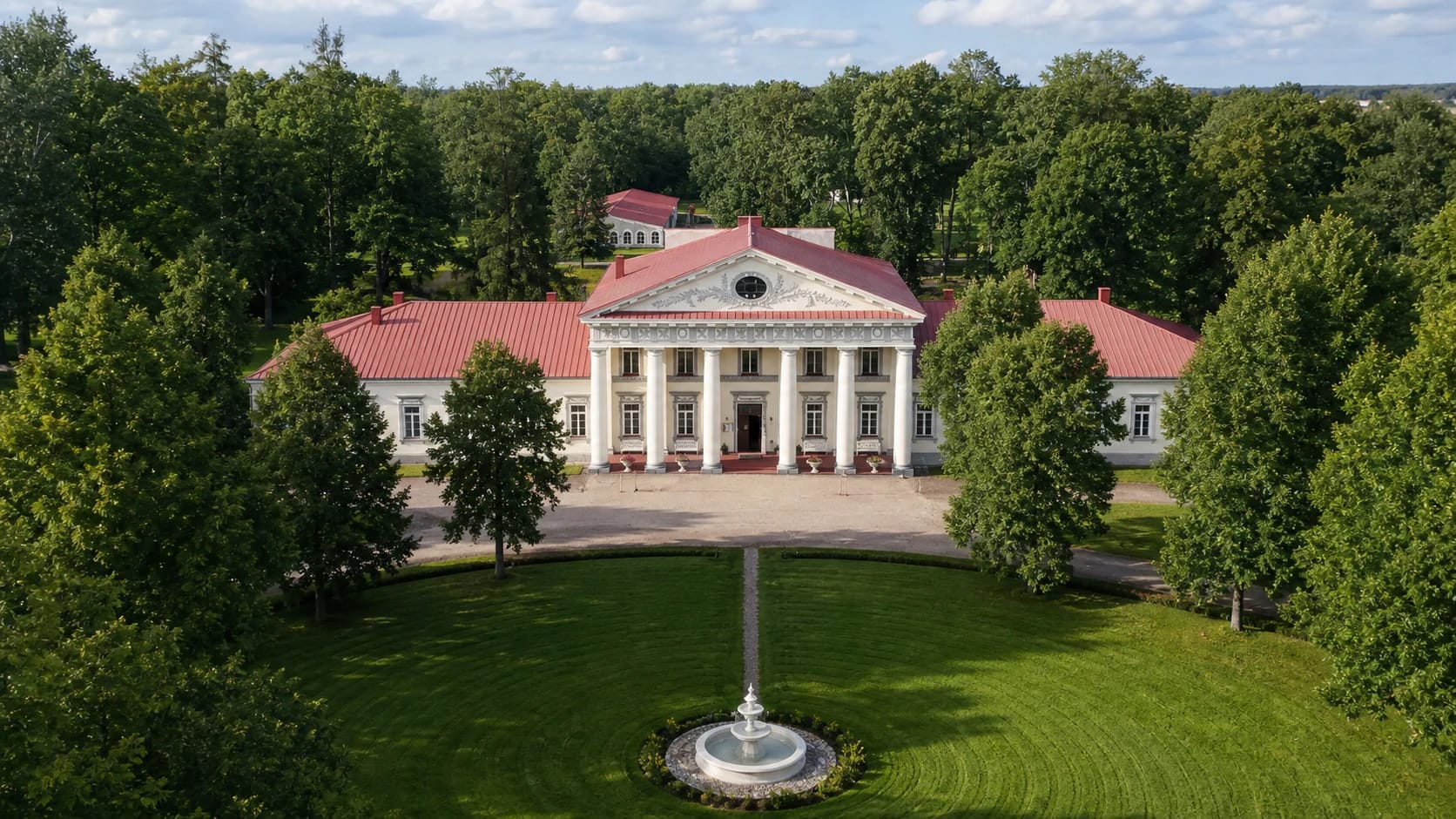 Taujėnai Manor palace with six-column portico, red roof, park trees, and fountain in front