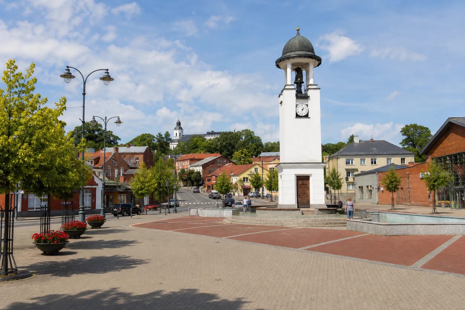 Telšių senamiesčio Turgaus aikštė su baltu laikrodžio bokštu, fontanu, raudonų ir pilkų trinkelių danga bei ant kalvos kylančia bažnyčia