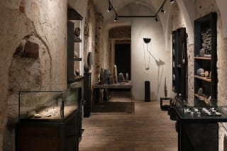 Vaulted Terra Recognita Gallery interior with dark stone and metal objects on pale plinths