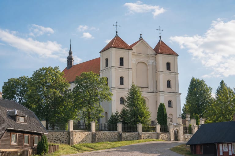 Trakų bazilikos kreminis dvibokštis fasadas, raudoni čerpių stogai ir šventoriaus vartai saulėtą vasaros dieną