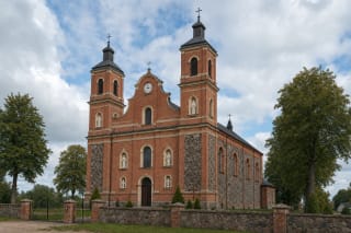 Краснокирпичная двухбашенная церковь в Тургелях с центральными часами, нишами для статуй и каменной оградой церковного двора