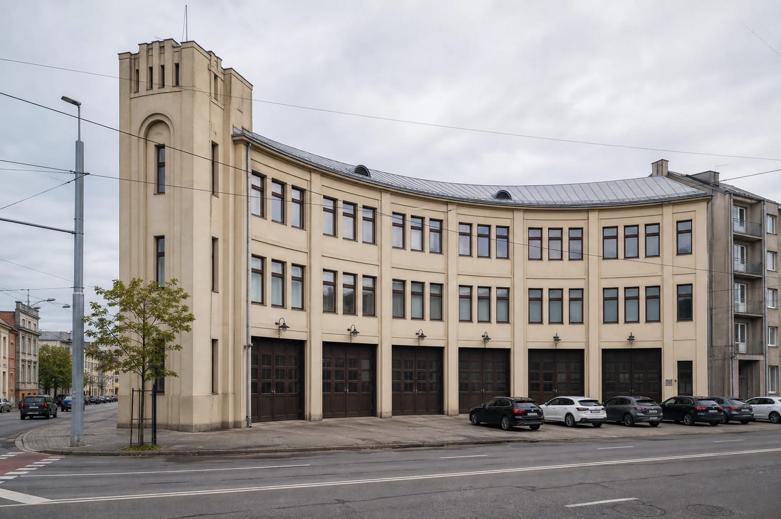 Curved light facade of the Firefighters' Palace in Kaunas with garage doors and a corner tower