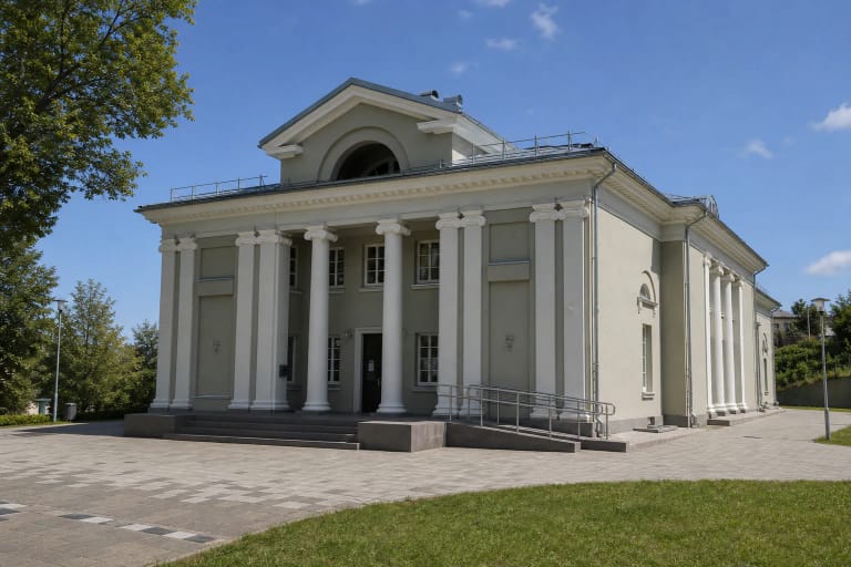 Ukmergės kraštotyros muziejaus simetriškas šviesiai pilkas buvusio kino teatro fasadas su kolonomis, frontonu ir įėjimo rampa