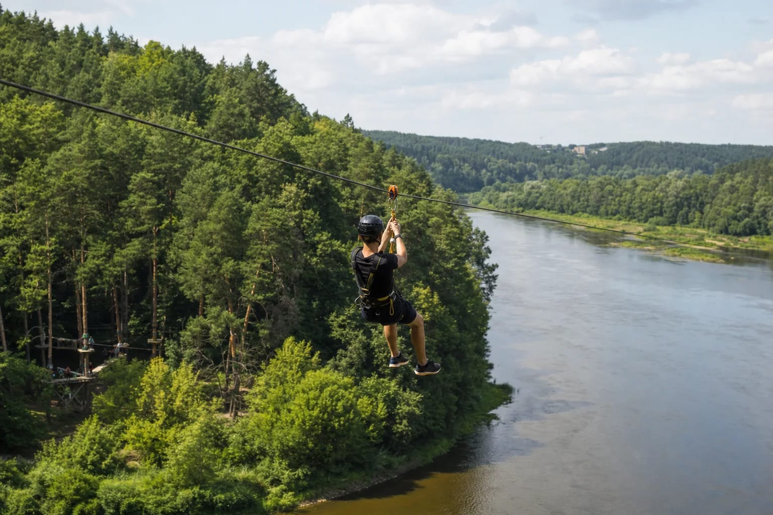 Harnessed visitor crossing the broad River Neris on an UNO Park Vilnius zipline above green Antakalnis woodland