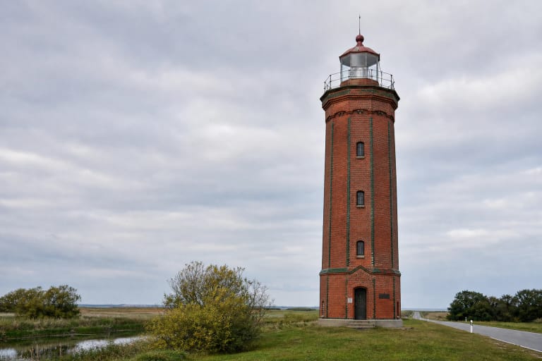 Uostadvario raudonų plytų švyturys Nemuno deltos polderių kraštovaizdyje su žaliais laukais ir vandens kanalais